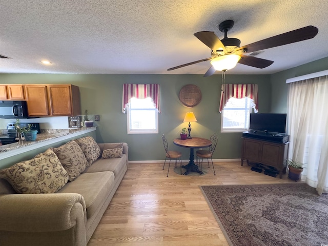 living room with ceiling fan, a textured ceiling, and light hardwood / wood-style flooring