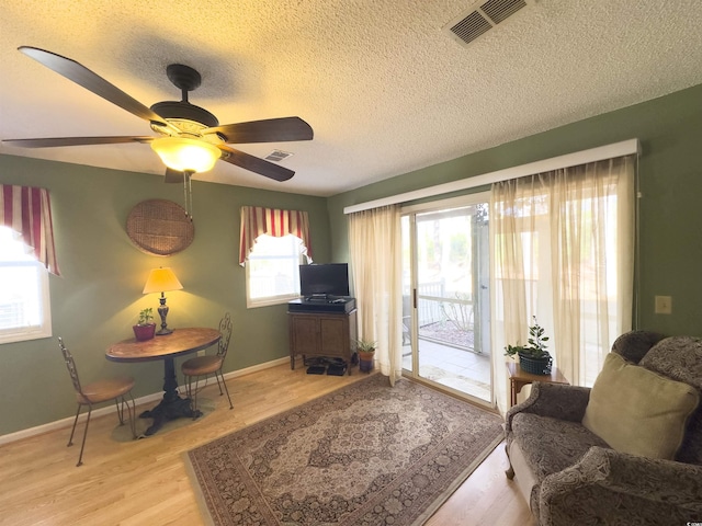 living room featuring ceiling fan, a textured ceiling, and light wood-type flooring