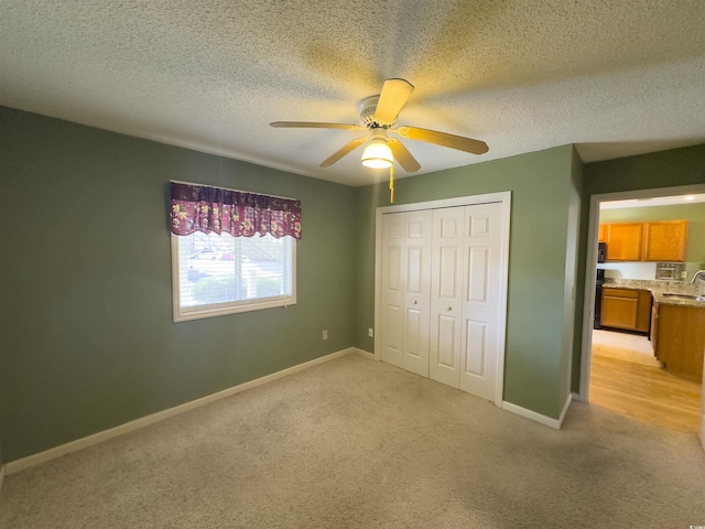 unfurnished bedroom with sink, ceiling fan, a textured ceiling, light colored carpet, and a closet