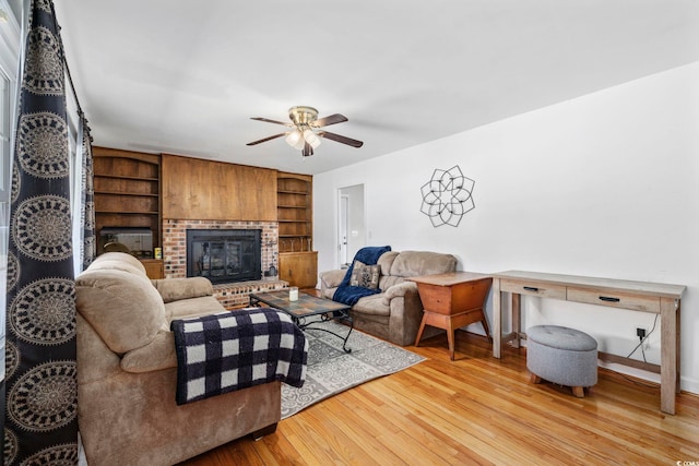 living room with built in shelves, a brick fireplace, ceiling fan, and light hardwood / wood-style flooring