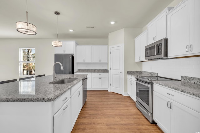 kitchen featuring hanging light fixtures, appliances with stainless steel finishes, a kitchen island with sink, and white cabinets