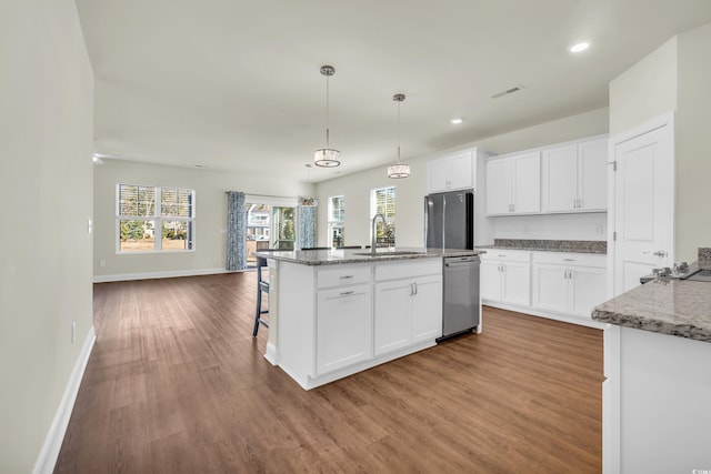 kitchen with stainless steel appliances, open floor plan, a kitchen island with sink, white cabinetry, and a sink