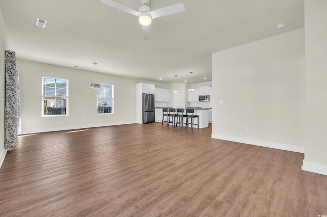 unfurnished living room featuring visible vents, ceiling fan, baseboards, and wood finished floors