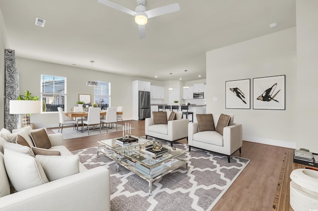 living area featuring baseboards, visible vents, ceiling fan, and wood finished floors