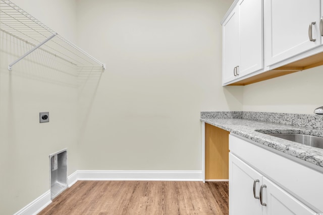laundry area featuring a sink, baseboards, cabinet space, light wood finished floors, and electric dryer hookup