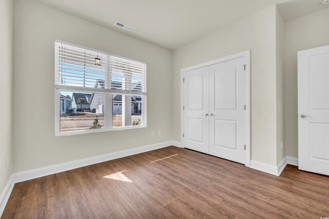 unfurnished bedroom featuring baseboards, a closet, visible vents, and wood finished floors