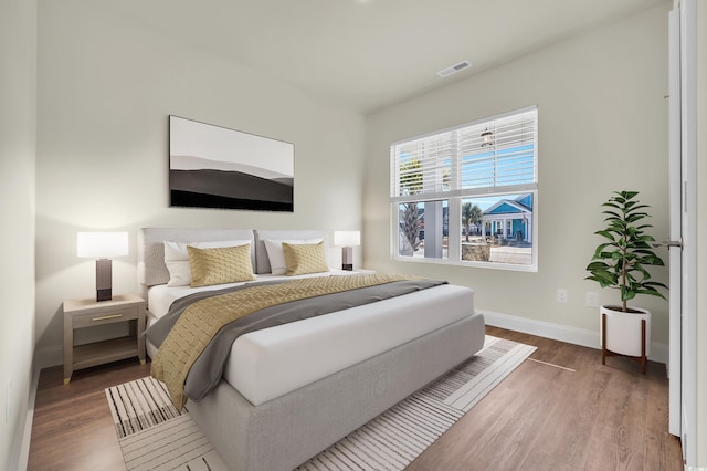 bedroom with baseboards, visible vents, and wood finished floors
