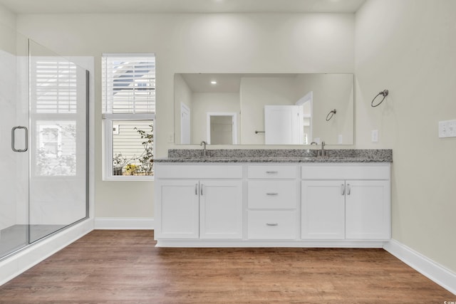 full bathroom featuring double vanity, wood finished floors, a shower stall, and baseboards