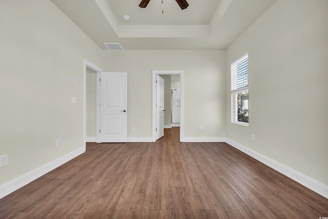 unfurnished bedroom with a raised ceiling, visible vents, baseboards, and wood finished floors