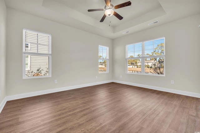 unfurnished room with visible vents, a tray ceiling, baseboards, and wood finished floors