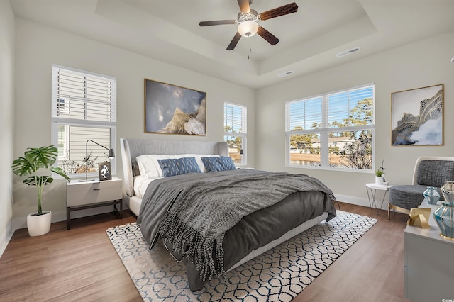 bedroom with wood finished floors, a ceiling fan, visible vents, baseboards, and a tray ceiling