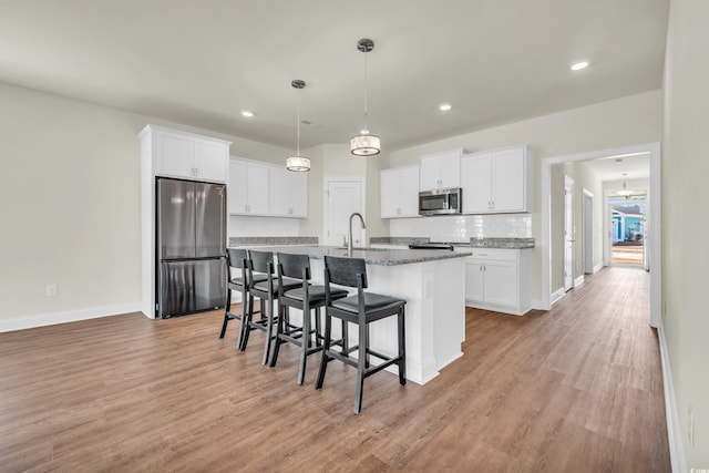 kitchen with white cabinets, a breakfast bar area, dark stone countertops, a kitchen island with sink, and stainless steel appliances