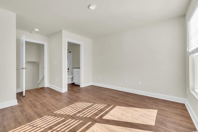 unfurnished bedroom with connected bathroom, baseboards, and wood finished floors