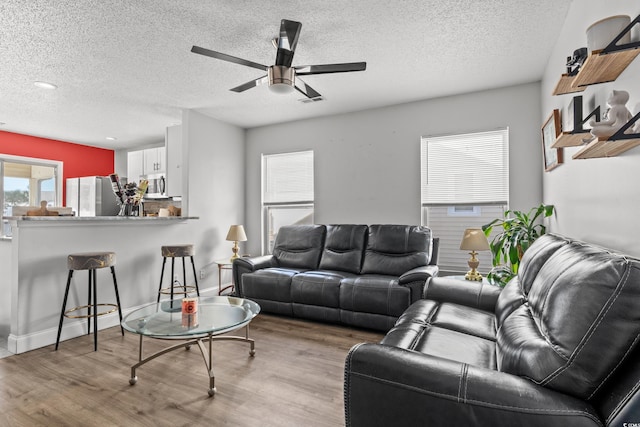 living room featuring ceiling fan, light hardwood / wood-style floors, and a textured ceiling