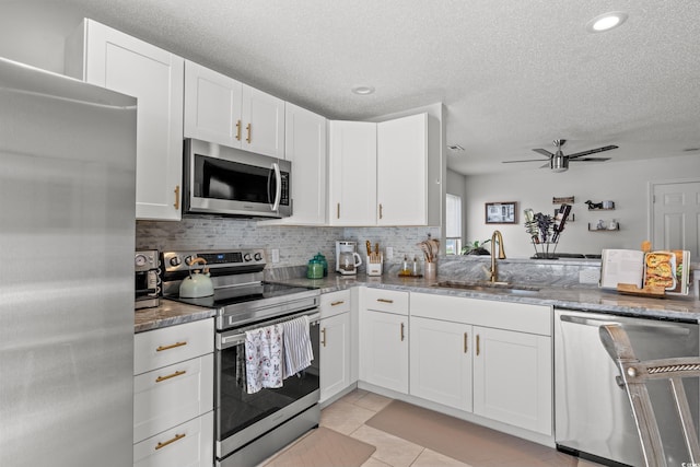 kitchen featuring stainless steel appliances, stone countertops, sink, and white cabinetry