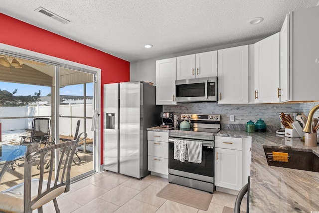 kitchen featuring stainless steel appliances, white cabinetry, light stone countertops, and light tile patterned floors