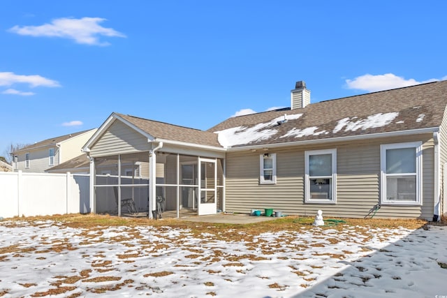 snow covered rear of property with a sunroom