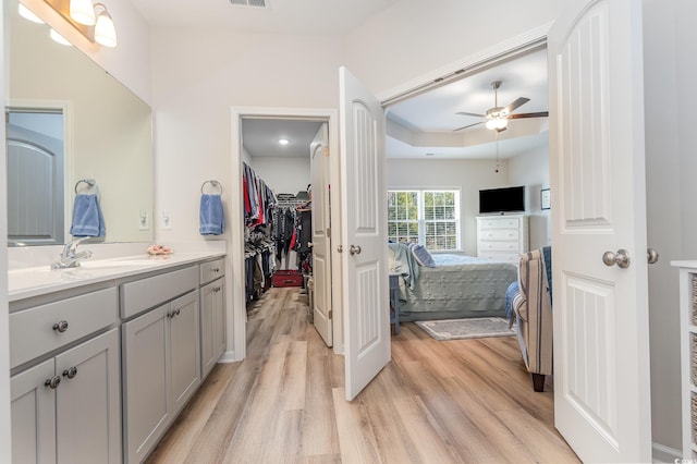 bathroom with hardwood / wood-style flooring, vanity, ceiling fan, and a tray ceiling