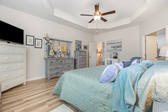 bedroom featuring ceiling fan, light hardwood / wood-style floors, and a tray ceiling