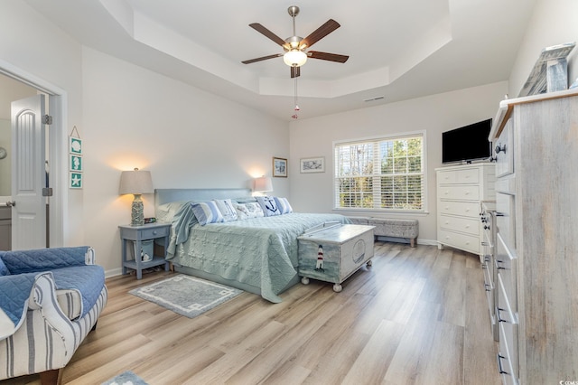 bedroom with ceiling fan, a tray ceiling, and light hardwood / wood-style flooring