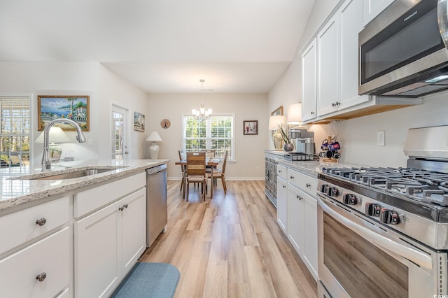 kitchen featuring sink, white cabinetry, decorative light fixtures, stainless steel appliances, and light stone countertops