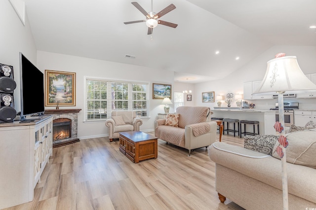 living room with vaulted ceiling, a stone fireplace, ceiling fan, and light wood-type flooring