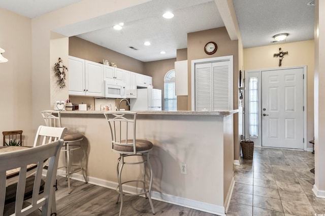 kitchen with a breakfast bar, white cabinets, white appliances, and kitchen peninsula