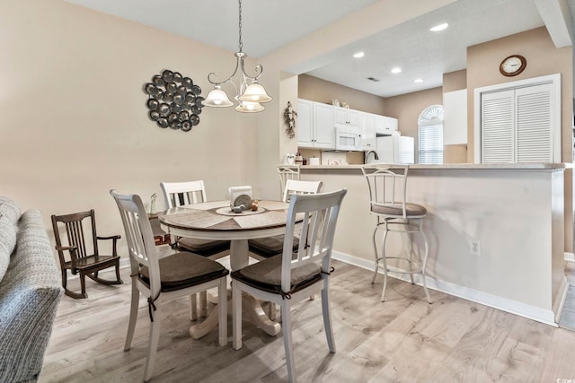 dining space with sink, light hardwood / wood-style flooring, and a notable chandelier