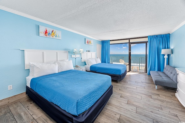 bedroom featuring ornamental molding, access to exterior, a water view, a textured ceiling, and light hardwood / wood-style flooring