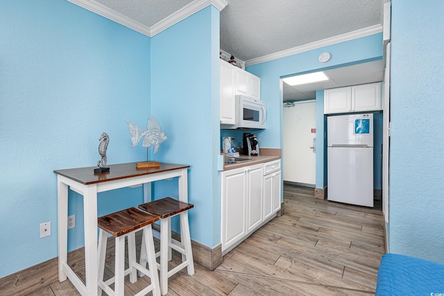 kitchen featuring crown molding, light wood-type flooring, white cabinets, and white appliances