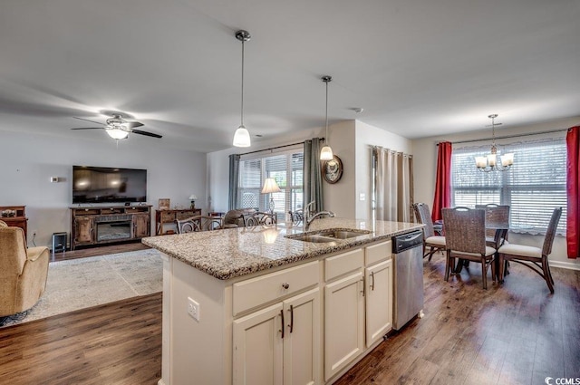 kitchen featuring sink, hanging light fixtures, light stone counters, a center island with sink, and stainless steel dishwasher