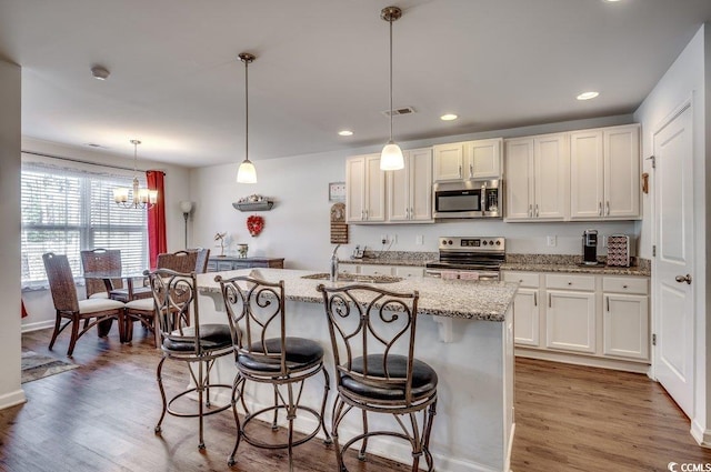 kitchen featuring pendant lighting, sink, white cabinets, stainless steel appliances, and a center island with sink