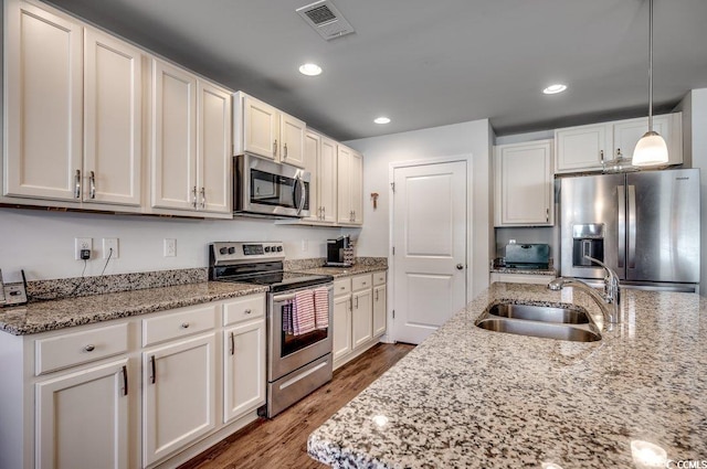 kitchen featuring sink, appliances with stainless steel finishes, white cabinetry, light stone countertops, and decorative light fixtures