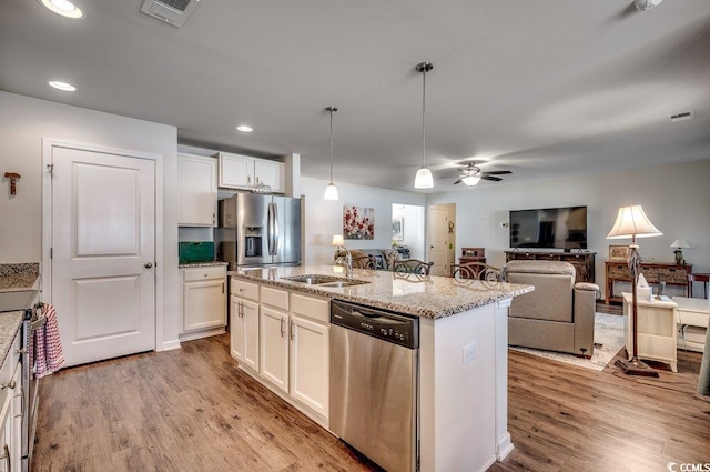 kitchen featuring decorative light fixtures, white cabinetry, an island with sink, sink, and stainless steel appliances