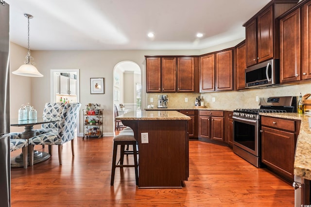 kitchen featuring pendant lighting, a kitchen breakfast bar, a center island, stainless steel appliances, and light stone countertops