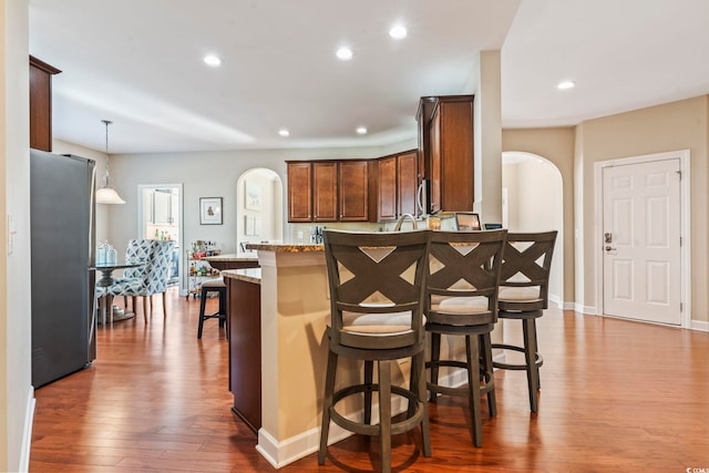 kitchen with dark wood-type flooring, a breakfast bar area, decorative light fixtures, stainless steel refrigerator, and light stone countertops