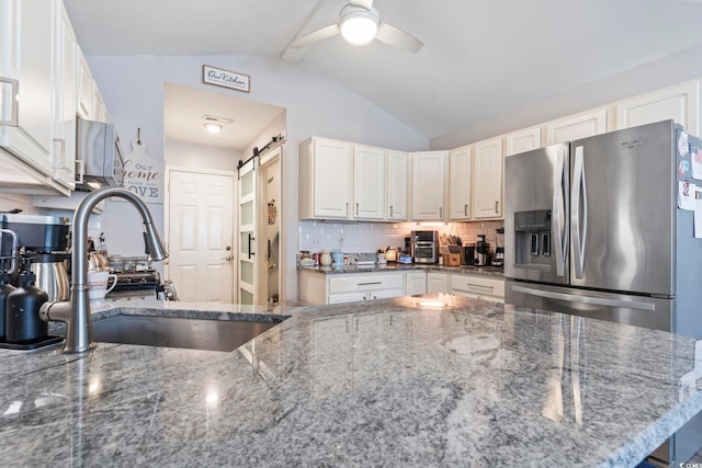 kitchen with white cabinetry, sink, dark stone counters, stainless steel refrigerator with ice dispenser, and a barn door