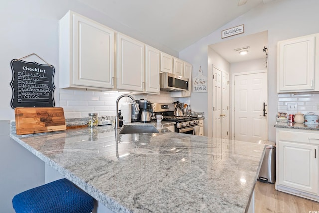 kitchen featuring appliances with stainless steel finishes, white cabinetry, backsplash, light stone counters, and kitchen peninsula