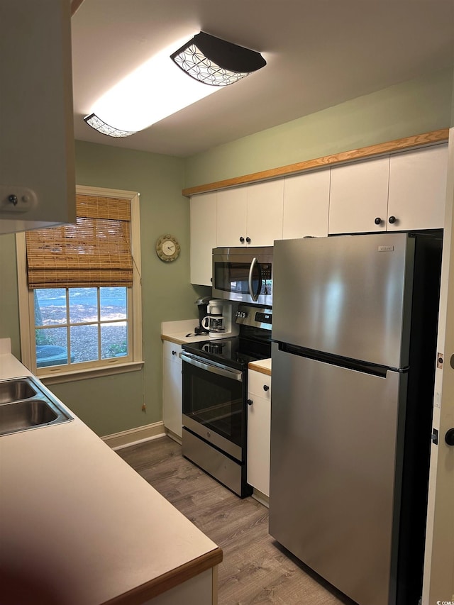 kitchen with appliances with stainless steel finishes, white cabinetry, wood finished floors, a sink, and light countertops