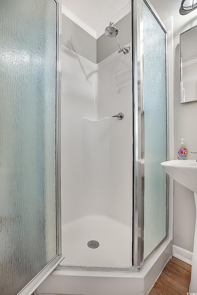 bathroom featuring hardwood / wood-style flooring, crown molding, a shower with door, and a textured ceiling