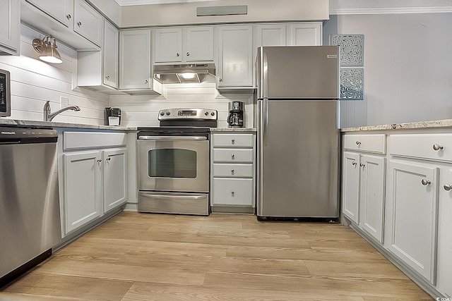 kitchen with white cabinetry, stainless steel appliances, light stone counters, ornamental molding, and light wood-type flooring