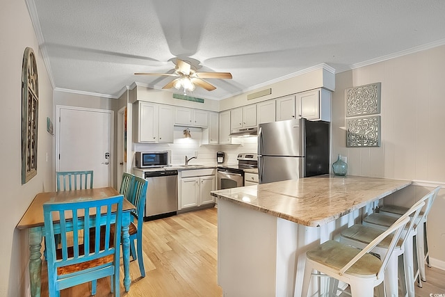 kitchen featuring sink, a breakfast bar area, appliances with stainless steel finishes, kitchen peninsula, and light wood-type flooring