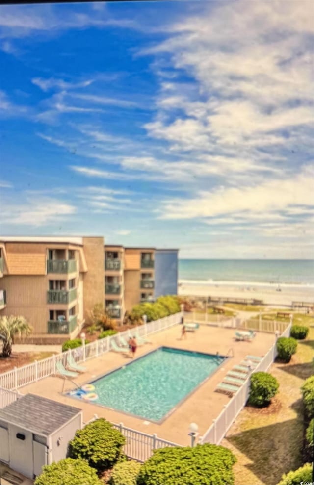 view of swimming pool featuring a patio, a water view, and a view of the beach