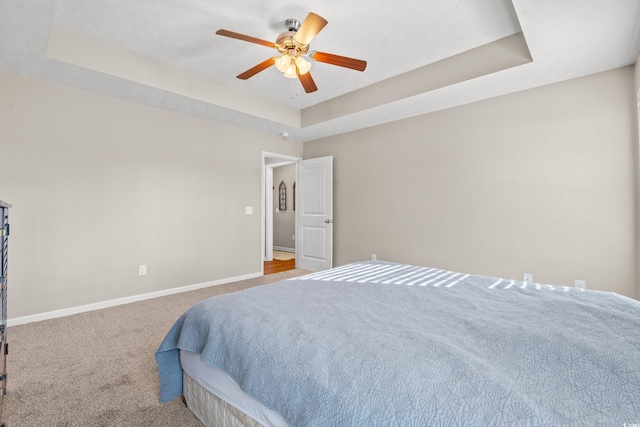 bedroom featuring a tray ceiling, a ceiling fan, baseboards, and carpet floors