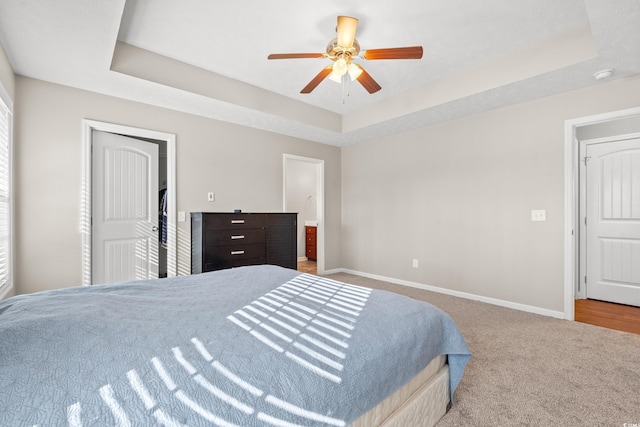 carpeted bedroom featuring a tray ceiling, baseboards, connected bathroom, and a ceiling fan