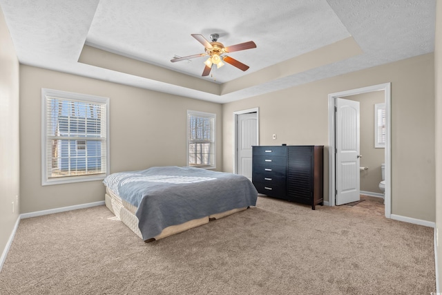 bedroom featuring light colored carpet, a raised ceiling, and baseboards