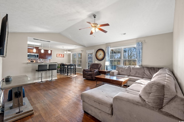 living area with visible vents, ceiling fan with notable chandelier, dark wood-style floors, baseboards, and lofted ceiling