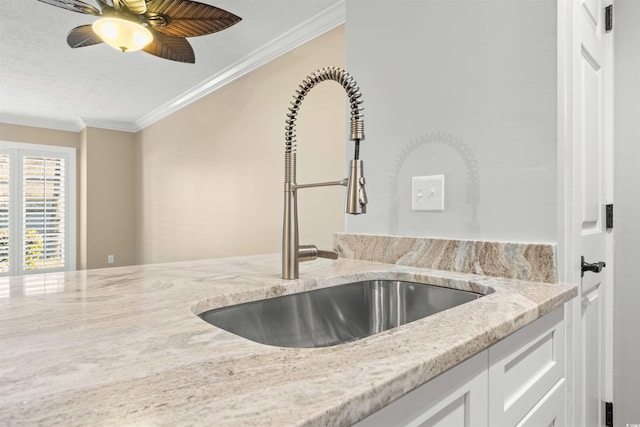 kitchen featuring sink, light stone counters, ornamental molding, ceiling fan, and white cabinets