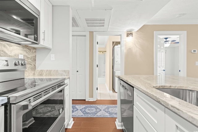 kitchen with crown molding, white cabinetry, stainless steel appliances, light stone countertops, and decorative backsplash