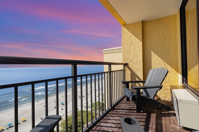 balcony at dusk featuring a water view and a beach view